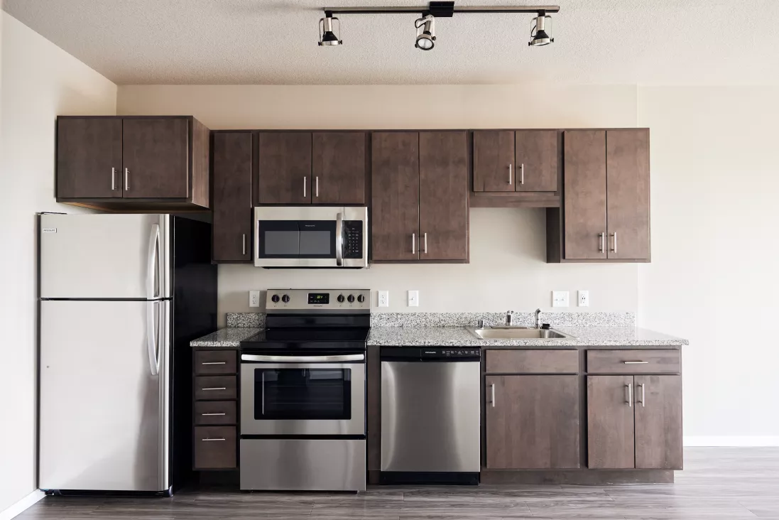 Modern kitchen with dark wood cabinets, light granite countertops, stainless steel refrigerator, microwave, oven, and dishwasher.
